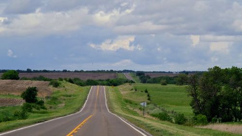 Road amidst grassy field against cloudy sky