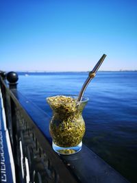 Close-up of drink by sea against clear blue sky