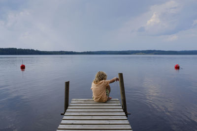 Rear view of woman on pier over lake against sky