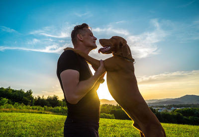 Rear view of woman with dog on field against sky