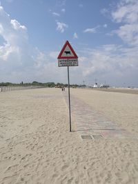 Road sign on beach against sky