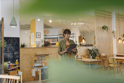 Female owner using digital tablet while standing in coffee shop