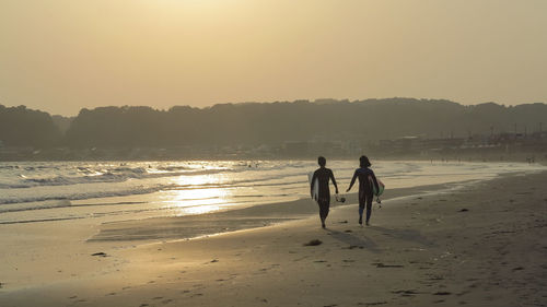 People on beach against clear sky during sunset