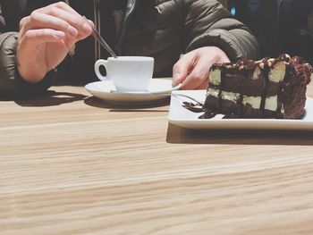 Midsection of man with coffee cup and cake on table