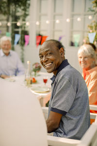 Side view portrait of smiling elderly man sitting at back yard