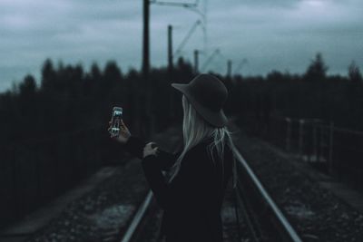Side view of woman taking selfie while standing railroad track