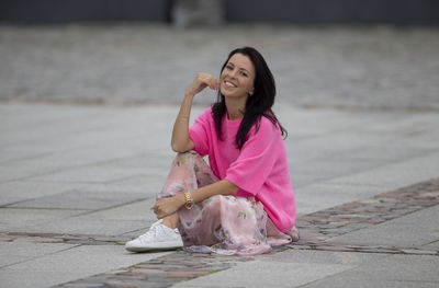 Portrait of young woman sitting on footpath