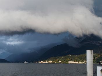 Scenic view of sea by mountains against cloudy sky