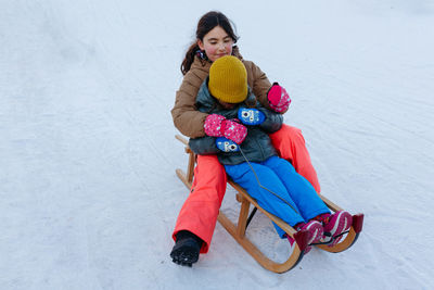 Two girls sledding on snow slope on wooden sled one child closes eyes with hands