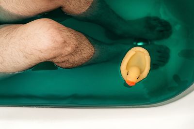 Low section of man by rubber duck in bathtub