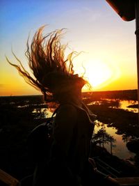 Rear view of woman by sea against sky during sunset