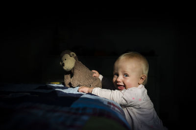 Portrait of cheerful girl playing with stuffed toy in darkroom