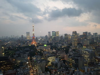 Aerial view of city lit up against cloudy sky