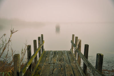 Wooden post on pier by sea against sky