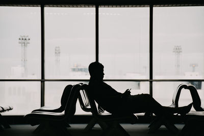 Silhouette man sitting by window at airport