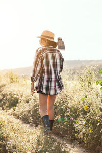 Rear view of farmer with axe wearing mask while walking by plants against clear sky