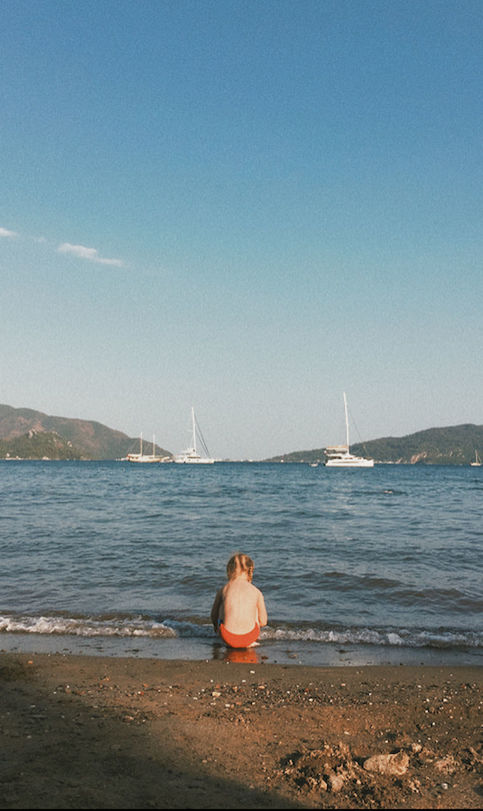 REAR VIEW OF MAN SITTING ON SHORE AT BEACH