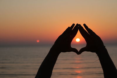 Silhouette hands making shape against sky during sunset