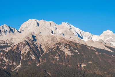 Low angle view of snowcapped mountains against clear blue sky