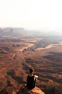 Rear view of woman sitting on rock against landscape