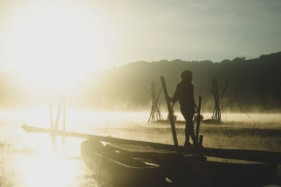 Rear view of silhouette man standing by lake against sky