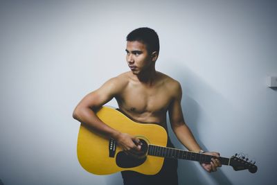 Young man playing guitar against wall