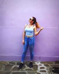 Full length portrait of young woman standing against wall