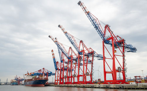 Cranes at commercial dock against sky