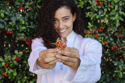 Portrait of smiling young woman holding berry against plants