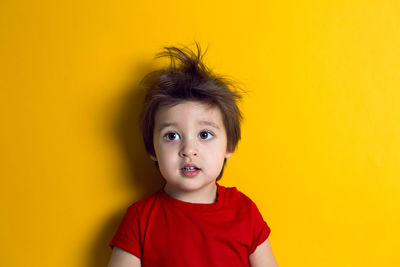 Cheerful baby boy in red t-shirt stands on yellow background