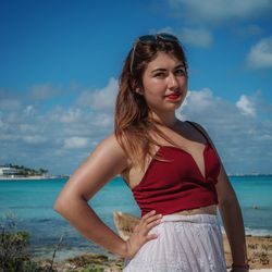 Beautiful young woman standing by sea against sky