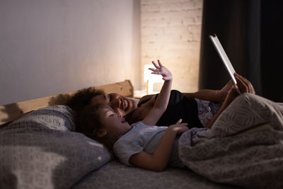 Happy ethnic mother and daughter making video call in evening