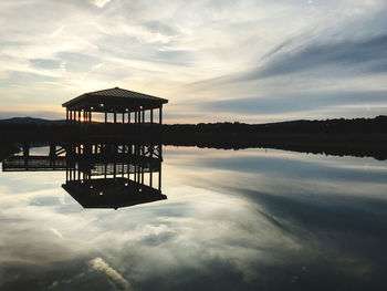 Silhouette built structure in lake against sky during sunset