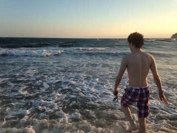 Rear view of shirtless man walking on beach against clear sky