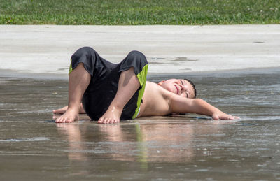 A young boy lies on the wet cement at a cooling off splash pad in michigan usa