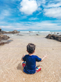 Rear view of boy on beach against sky