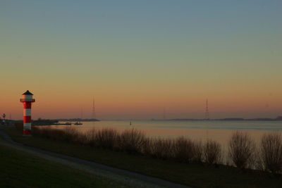 Lighthouse by sea against clear sky during sunset