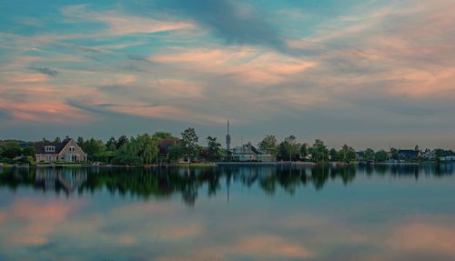 Scenic view of lake by building against sky during sunset