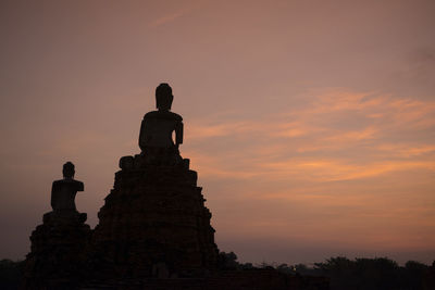 Low angle view of silhouette buddha statues against sky during sunset
