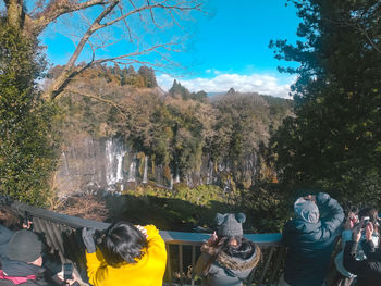 People photographing by trees in forest against sky