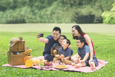 Happy family taking selfie while sitting on picnic blanket at park