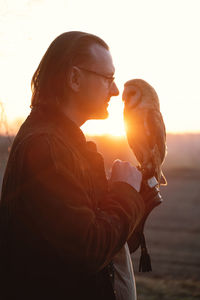 Man and wild bird over sunset sky in field looking on each other owl symbol of power, wisdom wealth