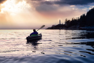 Man on boat in sea against sky during sunset