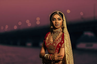 Portrait of beautiful bride wearing traditional clothing standing against sky