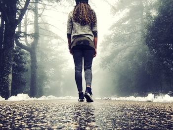 Rear view of woman walking on road at forest during winter
