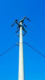 Low angle view of electricity pylon against clear blue sky