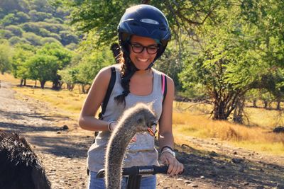 Smiling woman looking at ostrich against trees