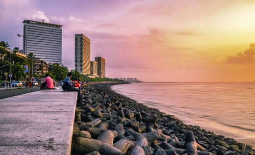 People on rock by sea against sky during sunset