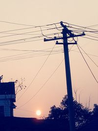 Low angle view of electricity pylon against sky during sunset