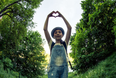 Low angle portrait of girl making heart shape standing amidst plants